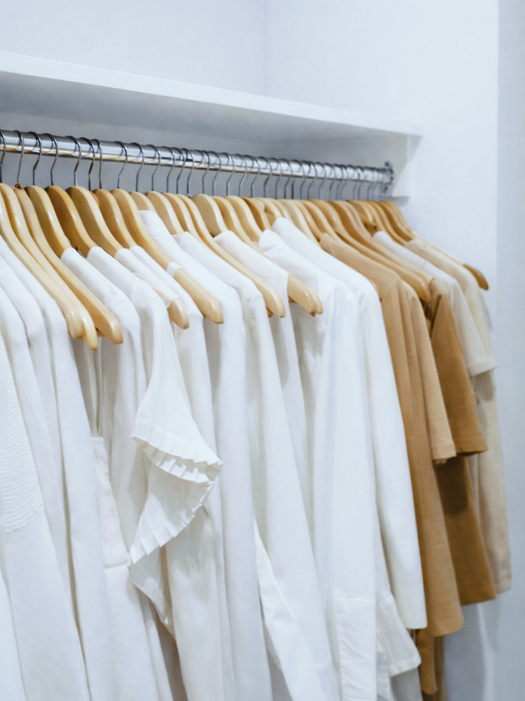 An organized closet with clothes sorted by color on wooden hangers